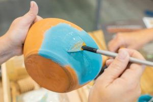 Mani che dipingono una ciotola di ceramica di blu, mettendo in mostra dettagli artistici e creatività.